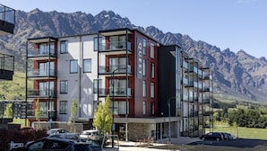 Un hotel de varios pisos con balcones, un estacionamiento y montañas al fondo.