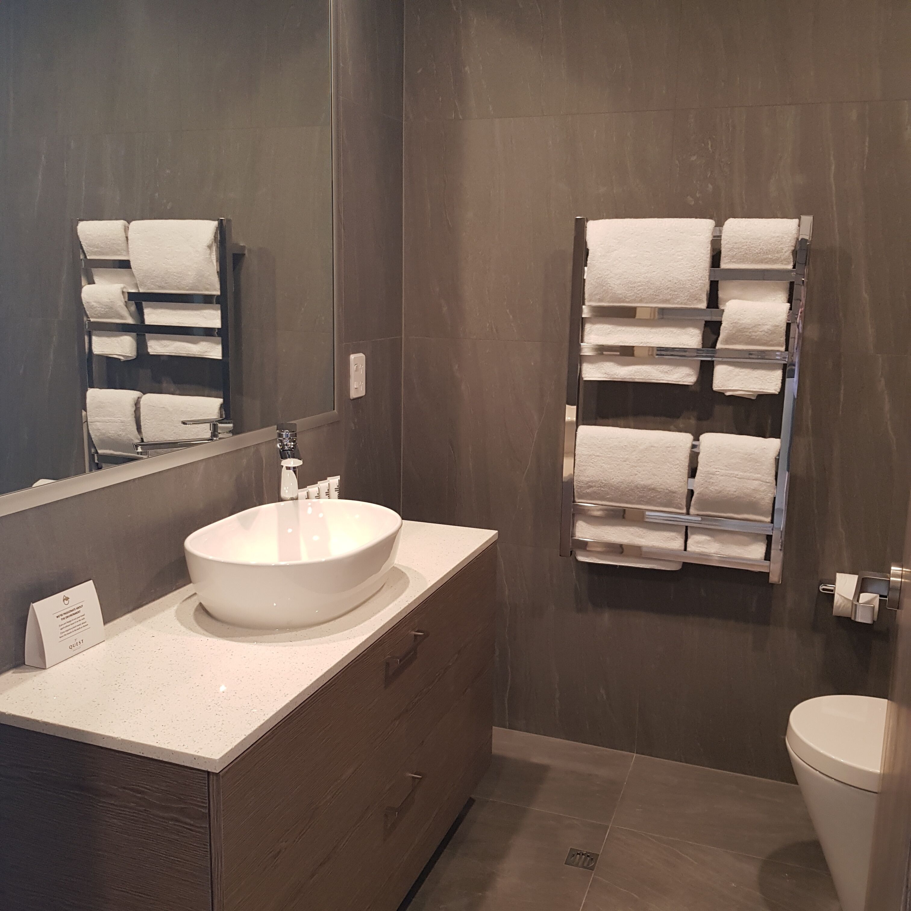 A modern bathroom with a large mirror, a round sink, and a towel rack.