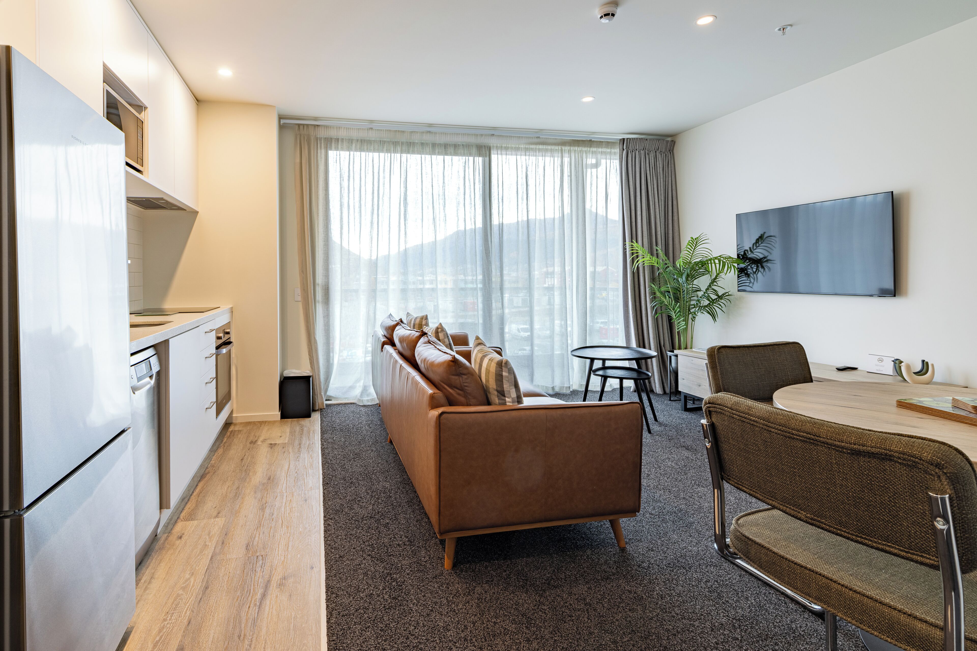 A modern living room with a sofa, a dining table, a TV, and a kitchen area.