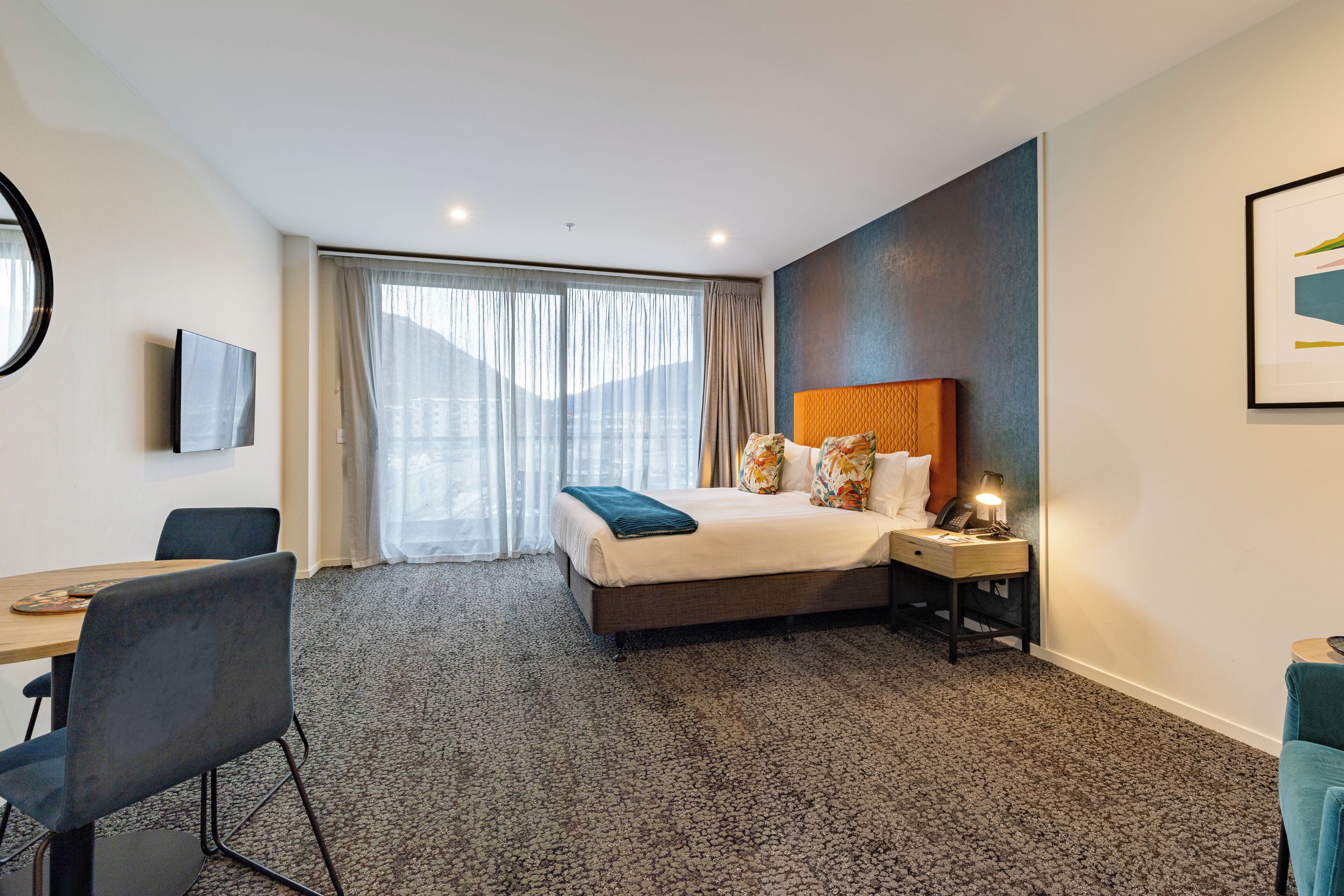 A hotel room with a bed, a desk, a chair, a TV, and a window with curtains.