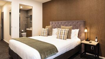 A modern hotel room with a large bed, a bedside table with a lamp, and a bathroom visible through an open door.