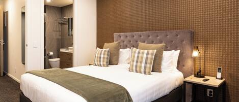 A modern hotel room with a large bed, a bedside table with a lamp, and a bathroom visible through an open door.
