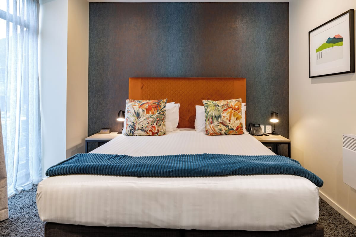 A hotel room with a large bed, two nightstands, a telephone, a lamp, and a framed picture on the wall.