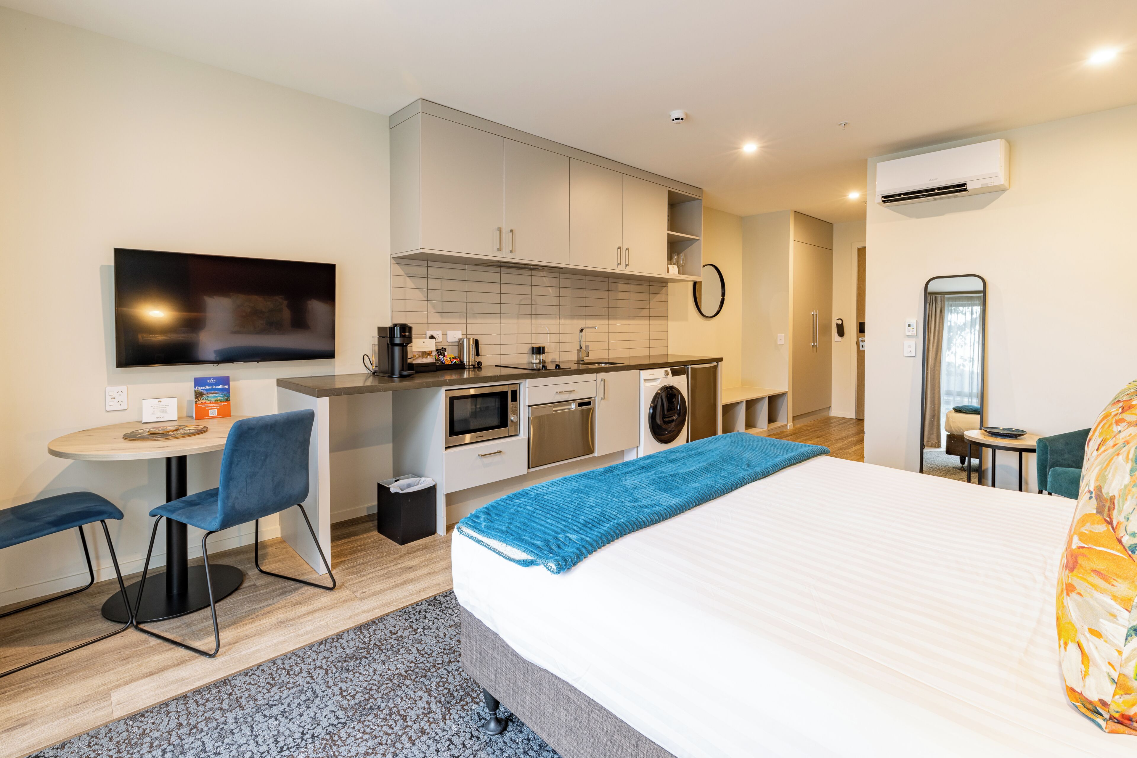 Una habitación de hotel moderna con cama, escritorio con silla, kitchenette y baño.