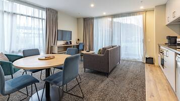 A modern hotel room with a dining area, a sofa, a TV, and a kitchenette.