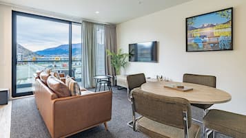 Una habitación de hotel moderna con un ventanal grande, un sofá, una mesa de comedor y un cuadro.