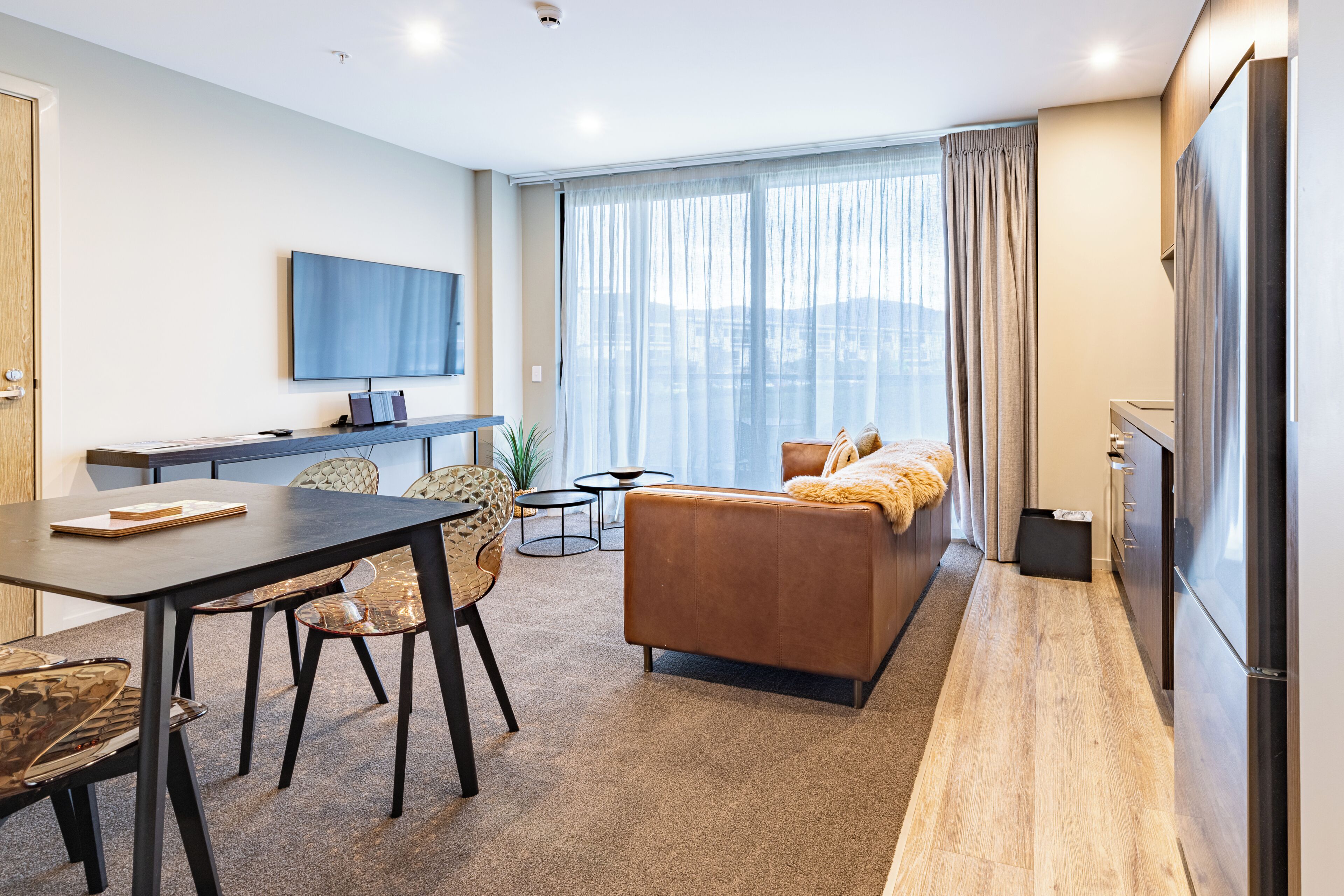 Una sala de estar moderna con sofá, mesa de comedor, sillas, televisor y un ventanal con cortinas.