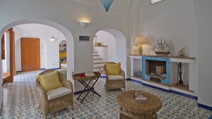 A spacious living area with wicker furniture, a fireplace, and a tiled floor. - Sweet Home (Praiano)