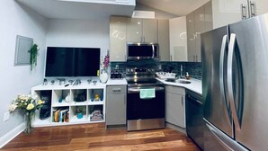 Uma cozinha moderna com eletrodomésticos de aço inoxidável, forno embutido e micro-ondas. Possui bancada branca e piso de madeira.
