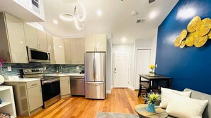 Cozinha moderna com eletrodomésticos de aço inoxidável, área de jantar com mesa e cadeiras, e sala de estar com sofá e mesa de centro.