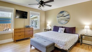 A bedroom with a bed, a bench, a ceiling fan, a TV, and a painting on the wall.