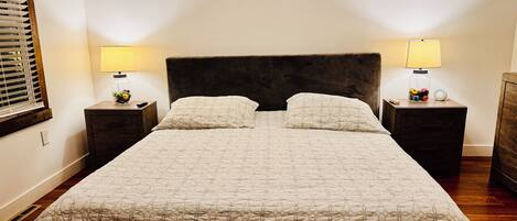 Una cama bien tendida con una colcha estampada y dos almohadas, flanqueada por dos mesitas de noche con lámparas y objetos decorativos.