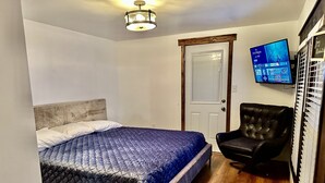 Ein Schlafzimmer mit Bett, Sessel, Fernseher und Tür.