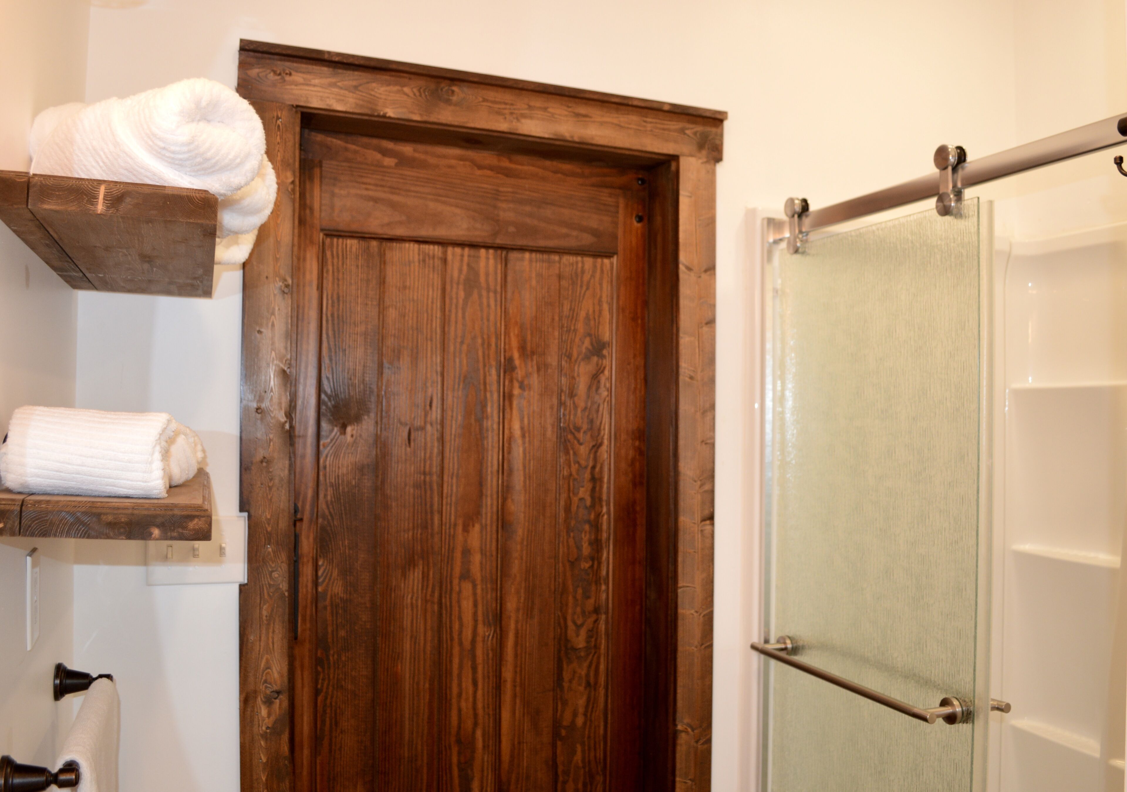 A wooden door with a towel rack above it, a glass shower door, and a towel hanging on the rack.