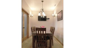 A dining area with a wooden table and chairs, a chandelier, wall-mounted lights, and a television on the wall. - Greystone Crossing Suite #12 (Heyburn)