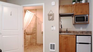 A bathroom with a shower, a toilet, and a sink. There is a microwave and a refrigerator in the kitchen area. - Greystone Crossing Suite #12 (Heyburn)