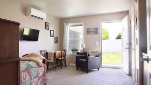 A cozy living room with a television, a dining table, and a comfortable chair. - Greystone Crossing Suite #12 (Heyburn)