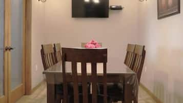 Un'area pranzo con un tavolo rettangolare, sei sedie, un lampadario, luci a parete, una TV a schermo piatto e un quadro appeso al muro.