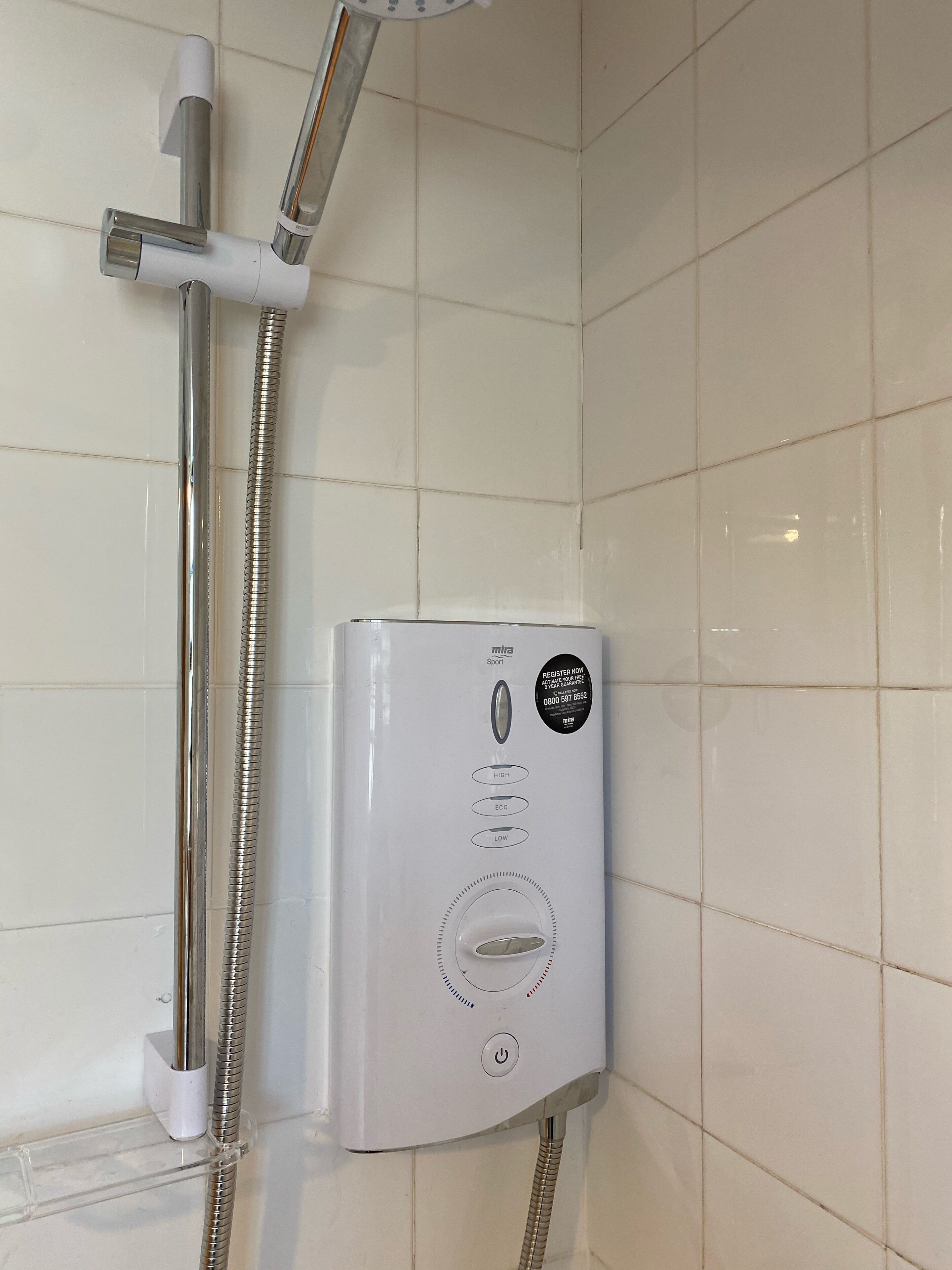 A white shower unit with a control panel, a handheld showerhead, and a flexible hose.
