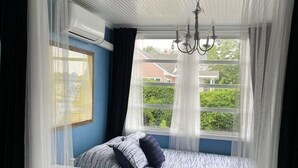 Een slaapkamer met een bed, een kroonluchter, een raam met gordijnen en een plafondventilator.