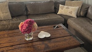 Een woonkamer met een bruine leren bank, een houten salontafel en een raam met gordijnen.