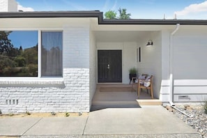 A modern house with a white exterior, a front door, a small porch with a bench, and a potted plant.