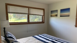 Une chambre à coucher avec un lit, une fenêtre avec des stores et deux tableaux accrochés au mur.