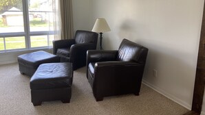 Un salon avec une grande fenêtre, un canapé, un pouf et une lampe.