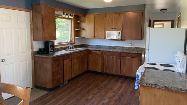 Une cuisine avec des meubles en bois, un réfrigérateur blanc, une cuisinière et une fenêtre donnant sur un paysage verdoyant.