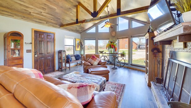 A spacious living room with leather sofas, a fireplace, and large windows offering a view of the outdoors. - Incredible Log Home: 1 Mile from Lake Tenkiller (Vian)