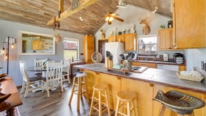 A kitchen with wooden cabinets, a central island with stools, a ceiling fan, and a deer head decoration. - Incredible Log Home: 1 Mile from Lake Tenkiller (Vian)
