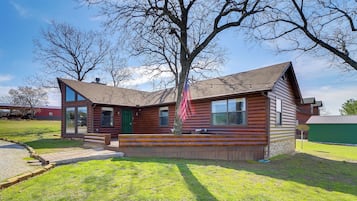 Cozy log cabin-style house with a large window and a green door, set amidst a well-manicured lawn and a tree.