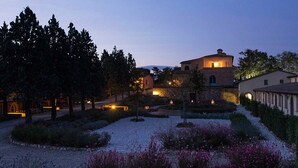 A well-maintained garden with pathways and flowering plants, a stone building with a round tower, and a small house with a visible window. - Villa Cielo - Cignella Resort Toscana (Toscana)