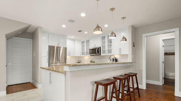 A modern kitchen with white cabinets, stainless steel appliances, and a central island with bar stools.