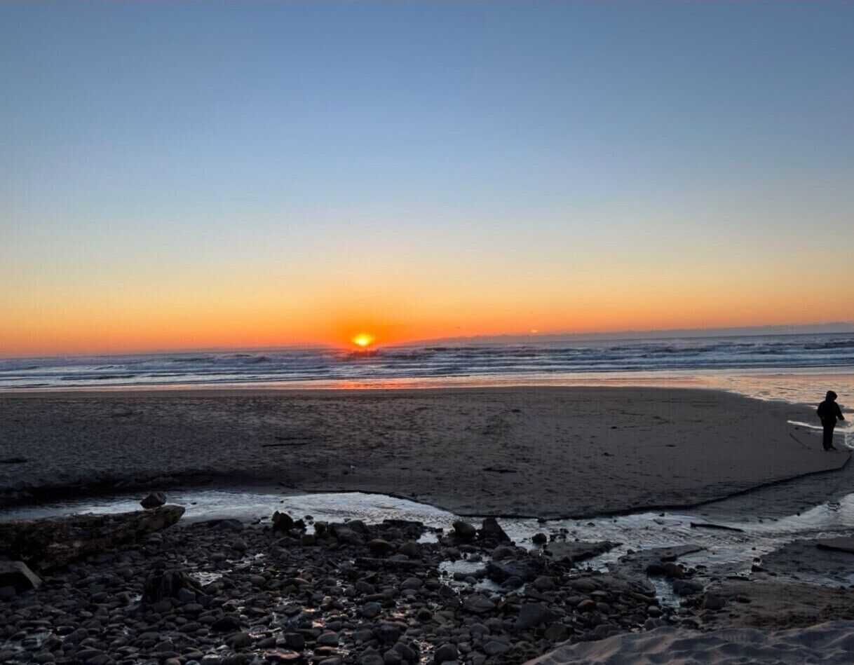 A beach at sunset with a person walking along the shore.