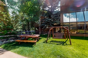 Relax in a serene outdoor space surrounded by lush greenery and a wooden fence, featuring a picnic table and a swing set.
