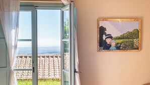 Habitació amb una finestra gran, un quadre a la paret i vista a un jardí i edificis a l'exterior.