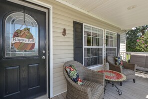 A porch with wicker furniture and a 'Happy Fall' sign on the door.