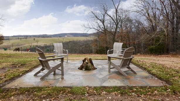 Een terras van natuursteen met twee Adirondack-stoelen gericht op een weids uitzicht over een grasveld en heuvels.