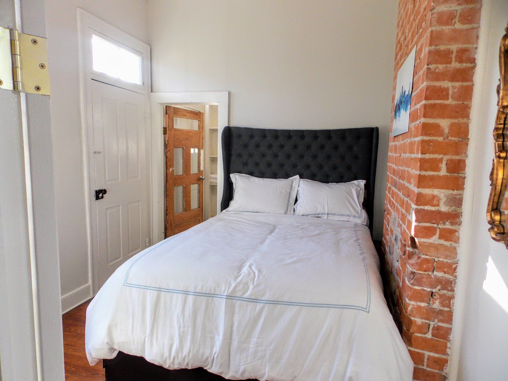 Een slaapkamer met een groot bed, een houten deur en een bakstenen muur.