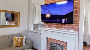 Ein Wohnzimmer mit Fernseher an einer Ziegelwand, Kamin, Sofa und Spiegel.