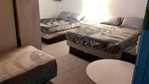 A small, compact room with two beds, a round table, and a white brick wall.
