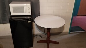 A compact kitchenette with a white microwave, a black refrigerator, and a small round table.