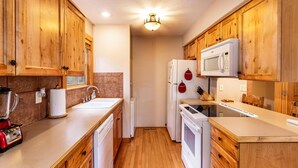 A compact kitchen with wooden cabinets, a microwave, a refrigerator, a sink, and a dishwasher. - Bear Cabin Getaway (Reeds Spring)