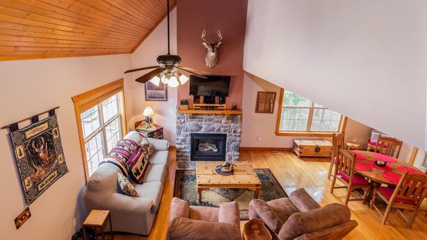 A spacious loft-style living room with a stone fireplace, a ceiling fan, and a mounted deer head. - Bear Cabin Getaway (Reeds Spring)