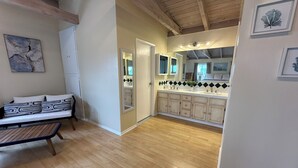 Un interno moderno con pavimento in legno, un divano con cuscini decorati, una cucina con piano di lavoro bianco e schienale a specchio e un'area pranzo con tavolo in legno.