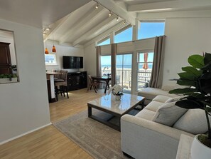 A spacious living room with a large window, a sofa, a coffee table, and a dining area with a TV. - BEACHFRONT PROPERTY! BEST L.A. LOCATION! (Los Angeles)
