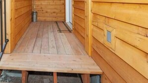 Een houten chalet met een smalle gang naar een deur, een klein raam en een aan het plafond bevestigd airconditioningsysteem.