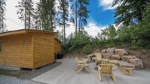 Une cabane en bois dotée d’un patio en béton, entourée d’arbres et de rochers.