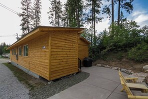 Una cabaña de madera pequeña con un porche, rodeada de árboles.